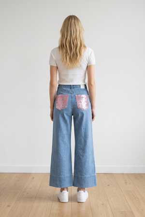 Jeans palazzo in denim chiaro, modello high-waist che valorizza il punto vita e slancia la silhouette. Il fondo ampio con risvolto strutturato dona un tocco di personalità. Questo jeans presenta passanti per cintura, chiusura frontale con zip e bottoni; classica struttura a 5 tasche di cui le due posteriori impreziosite da applicazione rosa brillante effetto gioiello.
