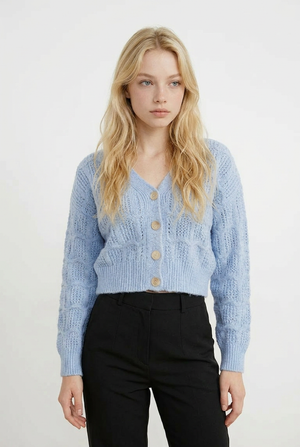 Cardigan CROP in maglia lavorata con raffinato motivo traforato a onde. Il design presenta uno scollo a V, chiusura frontale con 5 bottoni tono su tono e maniche lunghe con polsini e coste. 