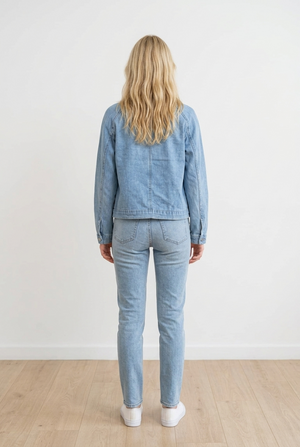 Giubbino in denim chiaro dal design moderno, caratterizzato da colletto ampio con revers stile biker, chiusura con zip asimmetrica, tasche decorative laterali e bottoni metallici sul colletto
