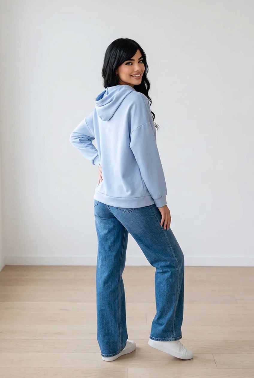 Felpa azzurra oversize indossata con cappuccio, coulisse a contrasto e patch decorativa sul braccio